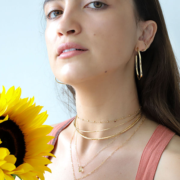brunette wearing layered gold choker necklaces a lemon quartz short gemstone necklace and brass maeve bold hoop earrings