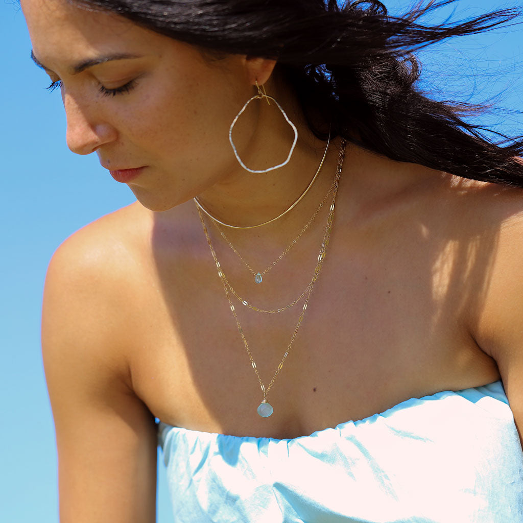 brunette on a blue top against wind looking down wearing 14k gold filled potatohead hoop earrings