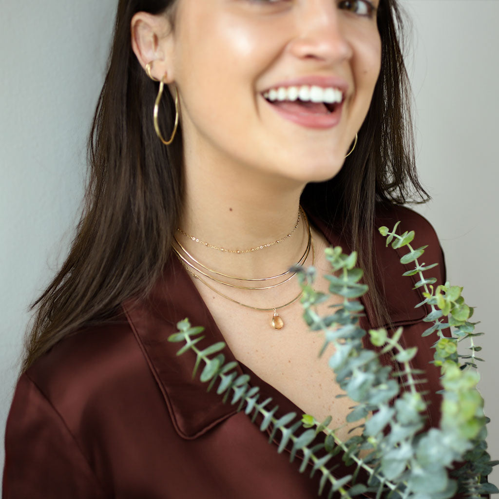 woman wearing 3 halo collars with a champagne quartz gemstone a ball chain choker necklace and maeve hoop earrings