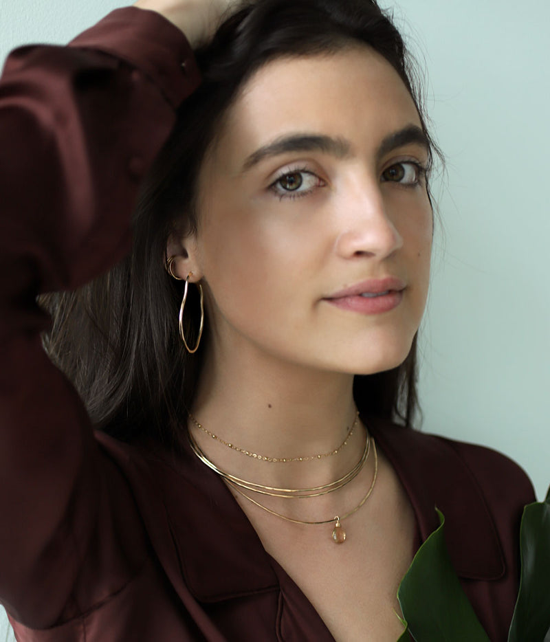 brunette wearing brass maeve thin hoop earrings champagne quartz gemstonce arc necklace and two 14k gold filled halo collars