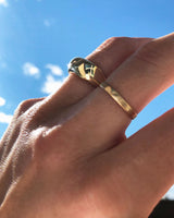 woman hand wearing curve ring on middle finger and hammered gold ring on ring finger against blue sky