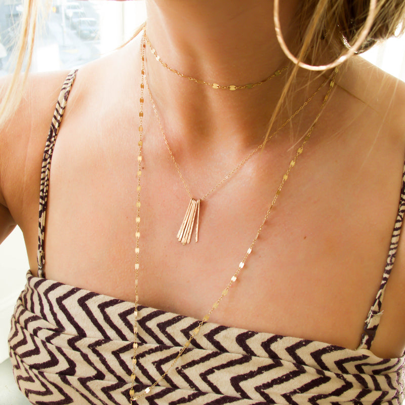 blond woman on a beige with brown stripes top wearing a 14k gold filled different strokes fringe pendant necklace