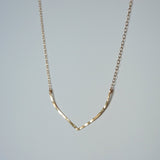 14k gold filled flight necklace on a grey surface partially reflecting light 