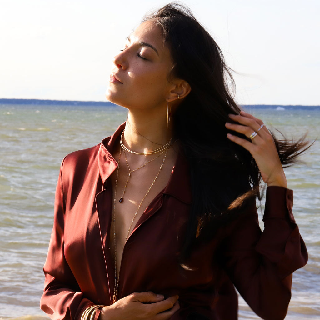 red blouse brunette wearing a garnet y gemstone necklace halo collars and 14k gold filled 2.5 inch thin hoop earrings