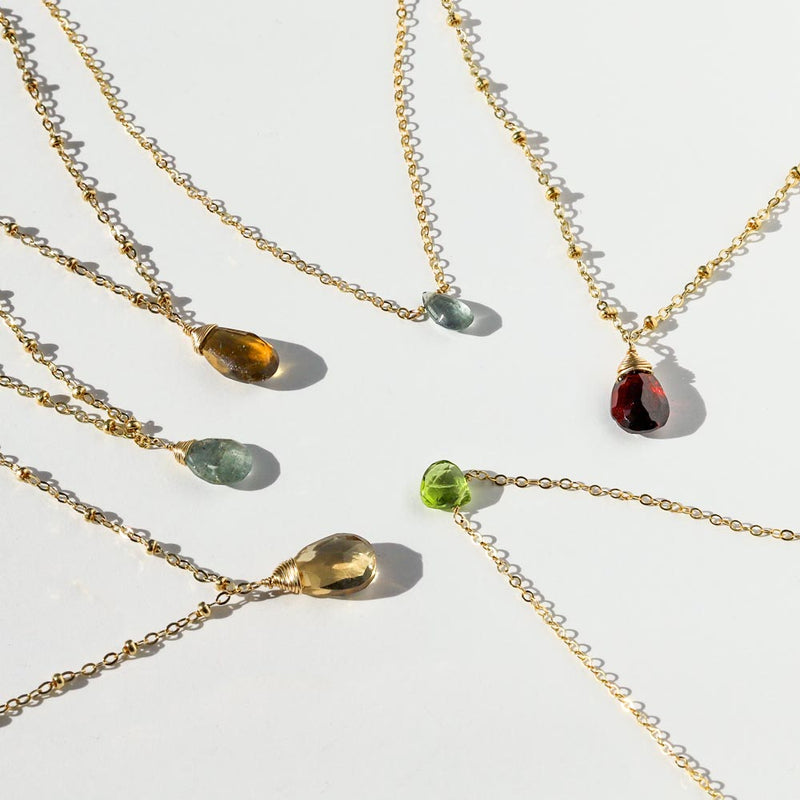 Beer moss aquamarine green amethyst champagne peridot and garnet beaded pendants and short gemstone necklaces on white surface