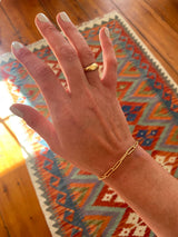 hand against colorful rug with chunky gold ring and thick gold chain bracelet