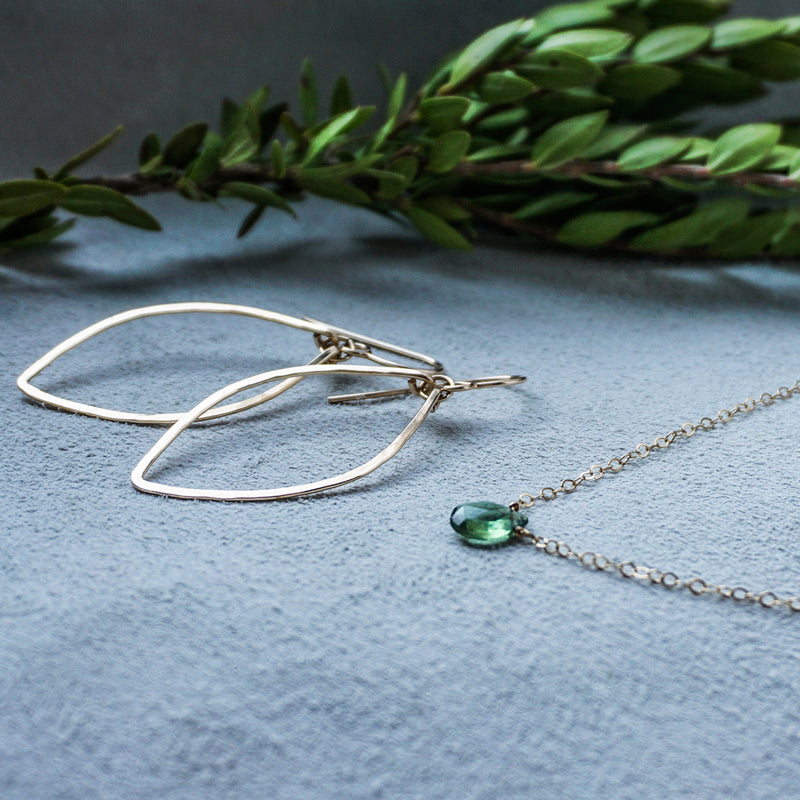 14k gold filled small leaf hoop earrings and green onyx short gemstone necklace on a gray surface next to a brand with leaves