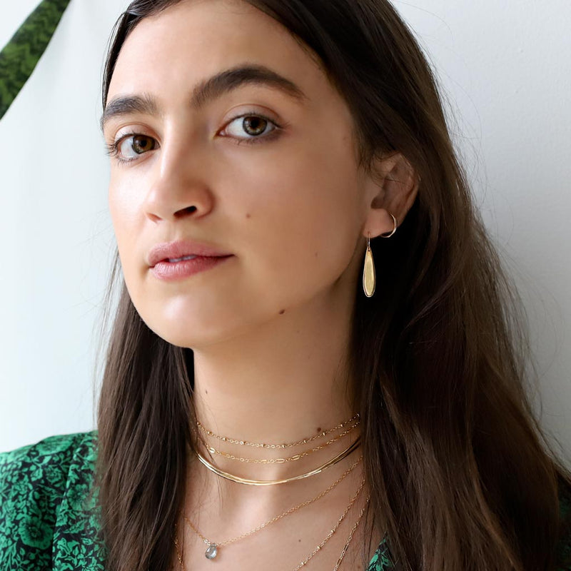 woman with small gold teardrop earrings and layered gold necklaces