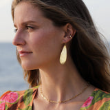 Woman wearing a hug hoop, Big drop shaped gold earring, and gold link necklace at the beach