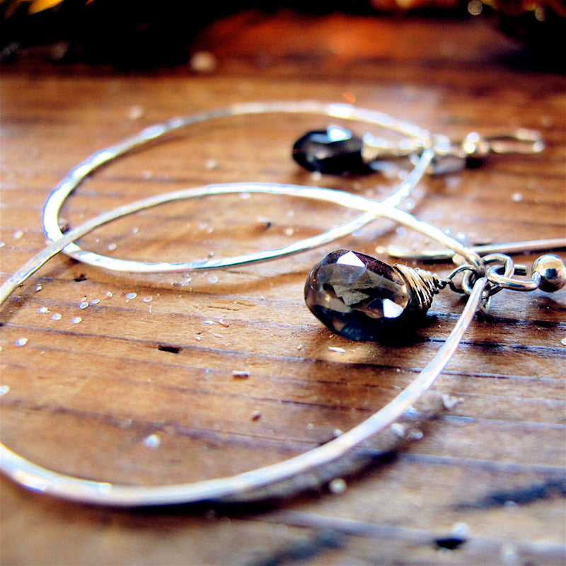 closeup of sterling silver smoky quartz silver gemstone drop hoops on a wood surface under direct light reflecting light