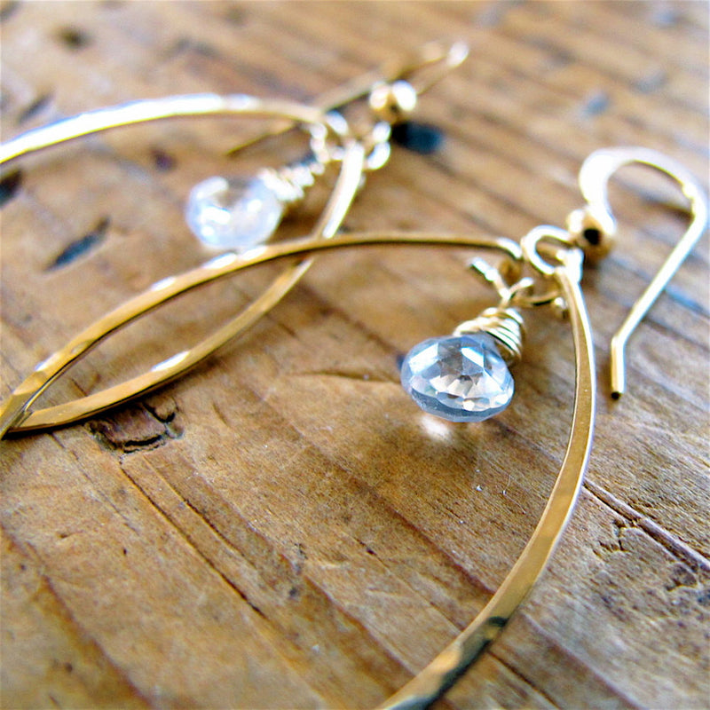 white topaz gemstone closeup of 14k gold filled white topaz gemstone drop hoops on a wood surface partially reflecting light