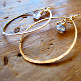 closeup of rose gold filled white topaz gemstone drop hoops laying on a wood surface partially reflecting light