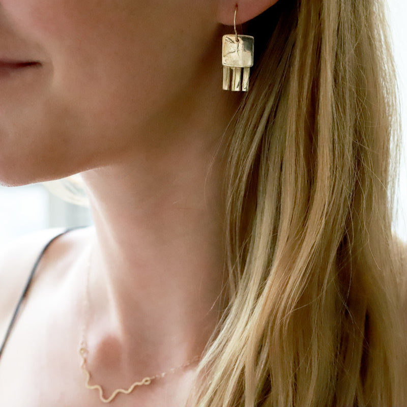 blond woman neck closeup wearing brass jellyfish drop earrings