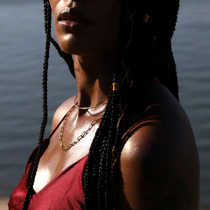 Black woman wearing two layered gold necklaces and a red blouse at the beach
