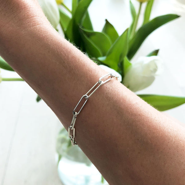 woman wrist wearing a sterling silver large link chain bracelet on a white tulips background