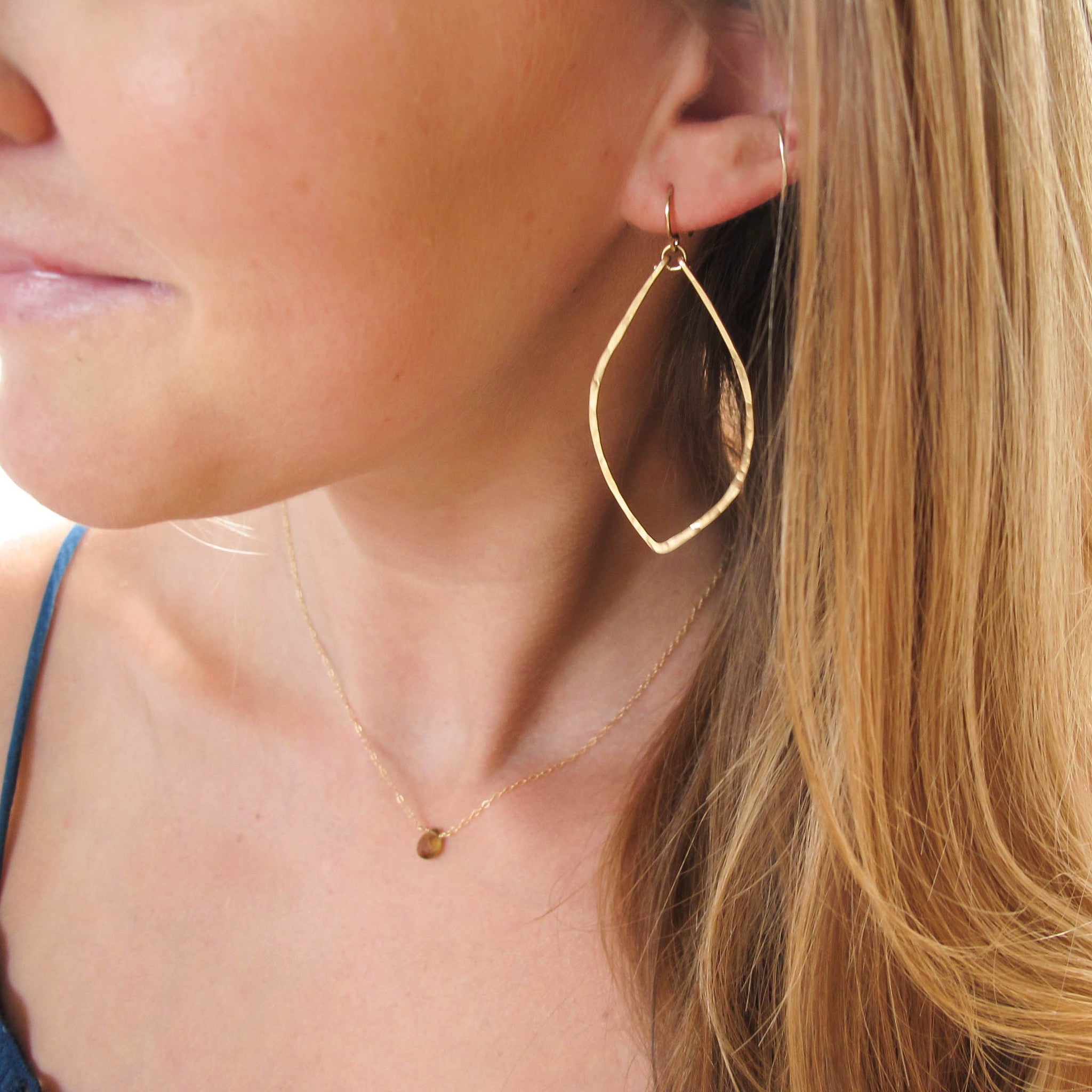 blond woman wearing 14k gold filled leaf hoop earrings on white surface 