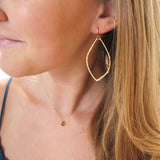blond woman wearing 14k gold filled leaf hoop earrings on white surface 