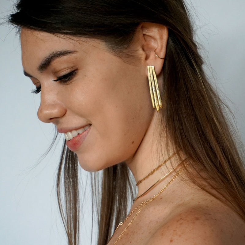 side shot brunette looking down wearing gold brass long fringe post earrings and a 14k gold fill cartilage hoop earring