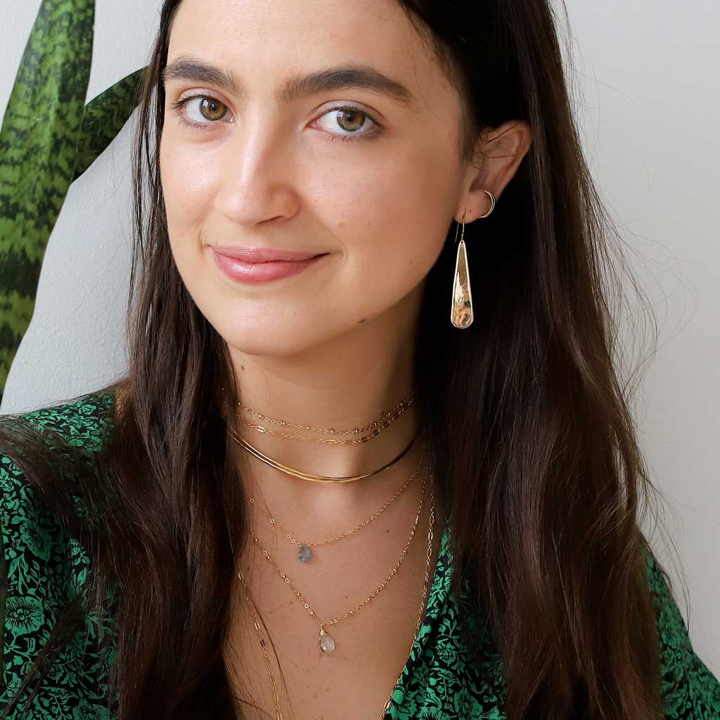 brunette wearing brass xl teardrop earrings green amethyst gemstone beaded pendant and moss aquamarine short gemstone necklace