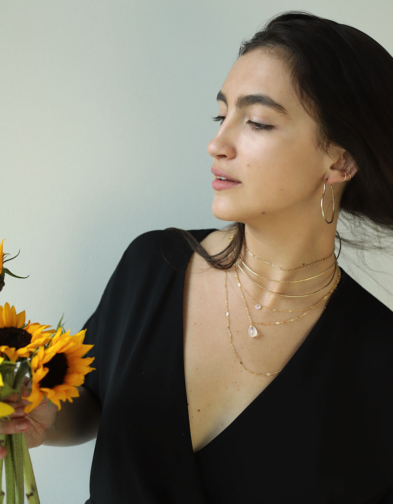 woman wearing brass maeve thin hoop earrings 14 gold fill moonstone short and choker wrap gemstone necklaces and halo collars
