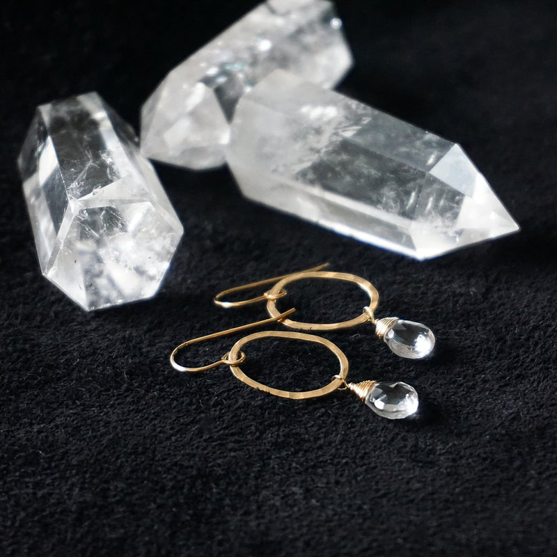 14k gold filled crystal quartz oval droplette gemstone earrings on a black surface next to quartz blocks