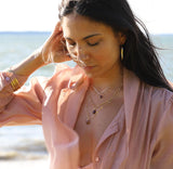 brunette at beach on a pink shirt against wind looking down wearing a 14k gold fill garnet short gemstone necklace