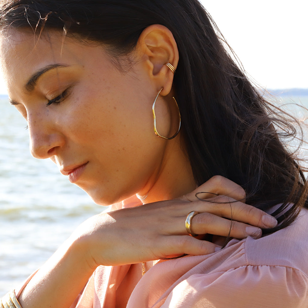brunette wearing brass with sterling posts maeve bold hoop earrings and 4k gold filled stacked cartilage hoop earrings