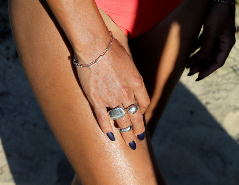 Woman wearing big silver rings, link bracelet and a bikini at the beach 