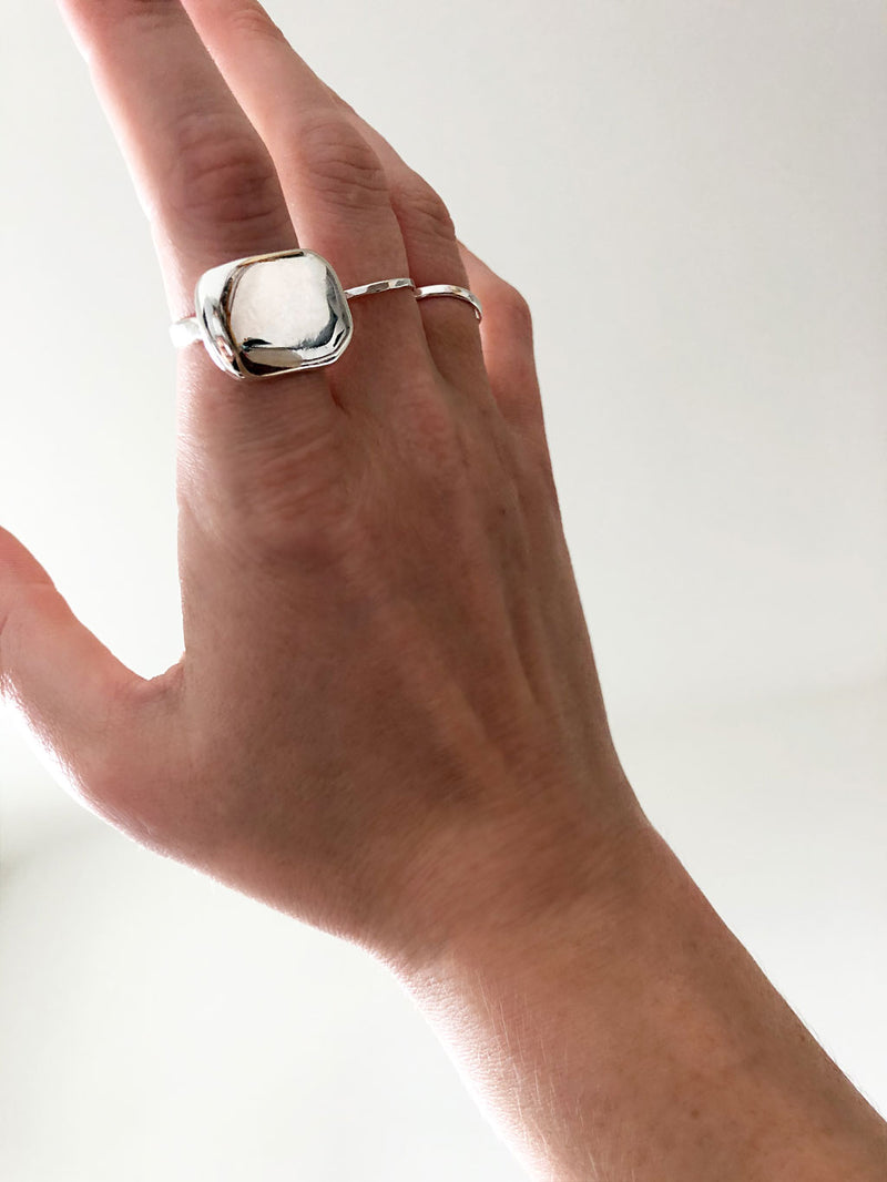 side view hand wearing plateau ring on index finger and hammered silver rings on middle and ring fingers on white background