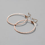 rose gold filled good people hoop earrings on a grey surface reflecting light