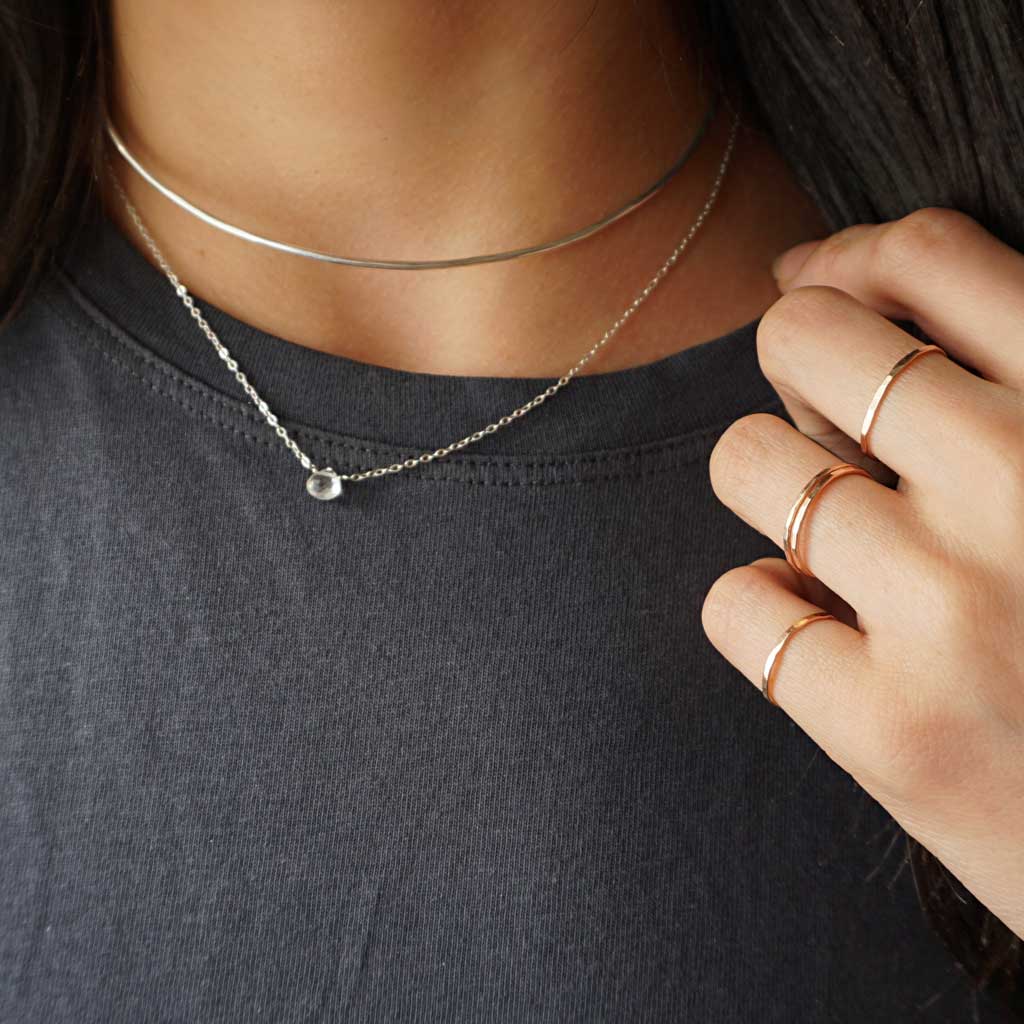 woman neck close-up wearing white topaz short gemstone necklace sterling silver halo collar and thin rose gold stacking rings