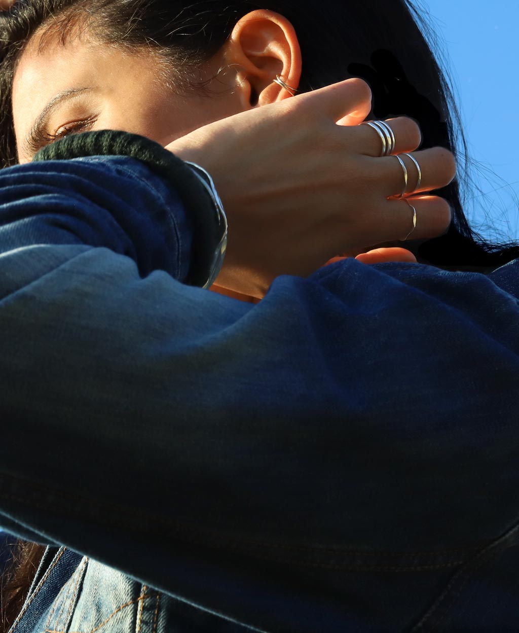 shot from below of a brunette on a jean jacket wearing sterling silver silver stacking rings on index middle and ring fingers