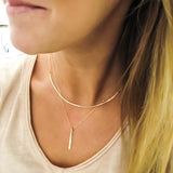 blond woman on a beige v neck wearing a 14k gold filled single stroke necklace