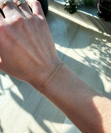 woman hand wearing thin gold stacking rings on middle and ring fingers and a 14k gold filled small link chain bracelet