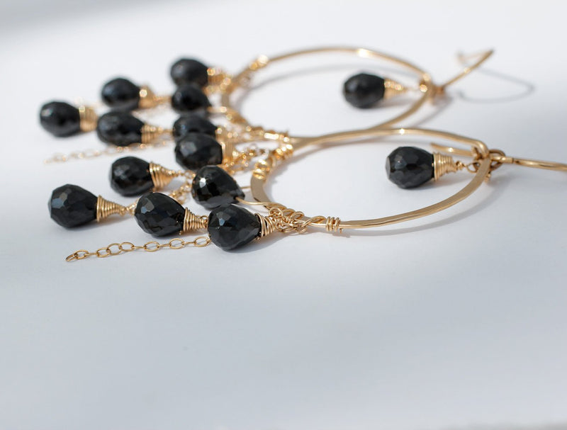 black spinel closeup of 14k gold filled black spinel cascade gemstone hoops laying on a grey surface