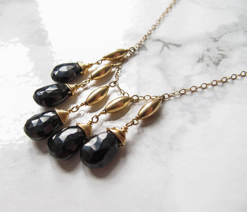 closeup of a 14k gold filled black spinel cascade gemstone necklace laying on a shiny white surface 
