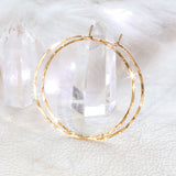 14k gold filled 2 inch endless thin hoop earrings laying on crystal quartz under a shiny bright light on white surface
