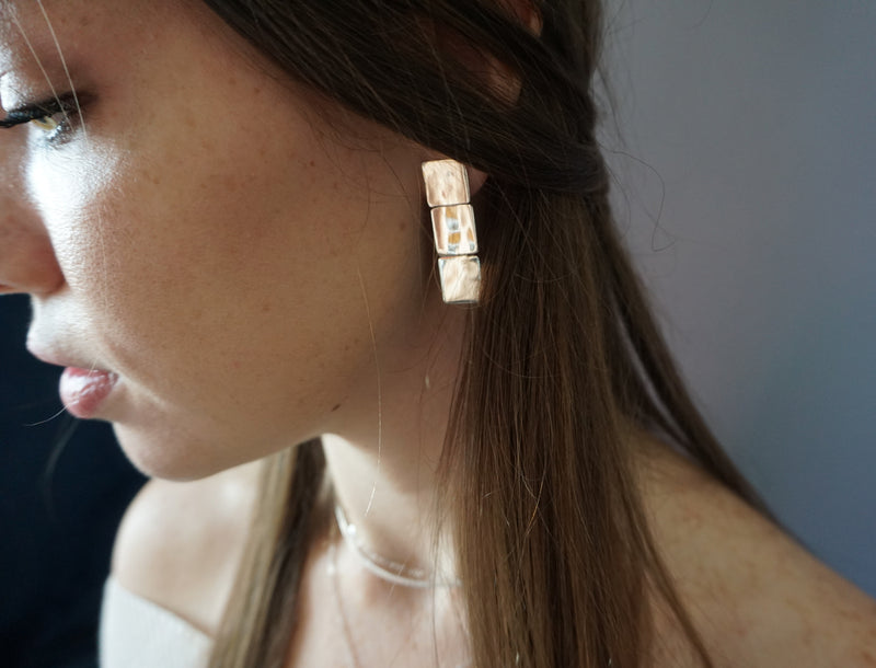 brunette looking down side face closeup wearing gold brass three square post earrings
