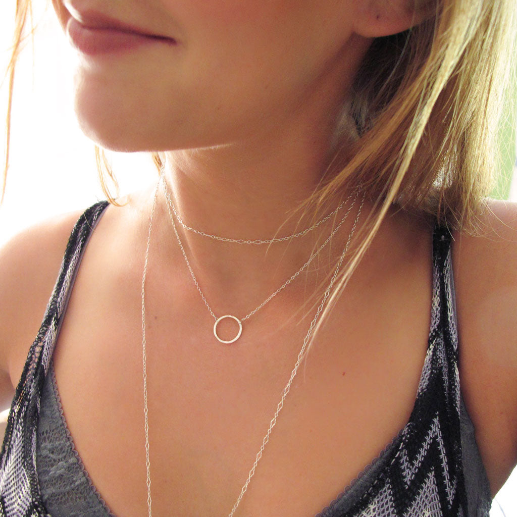 girl with delicate silver circle necklace and layered dainty silver chains