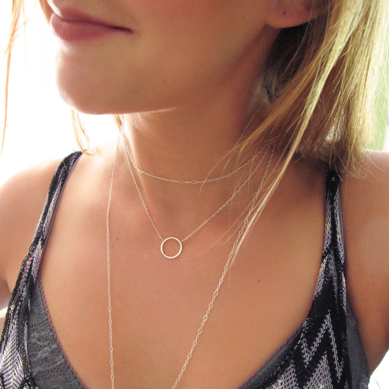 girl with delicate silver circle necklace and layered dainty silver chains