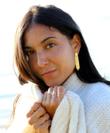 brunette wearing a white wool sweater with gold brass long fringe post earrings on a shiny day