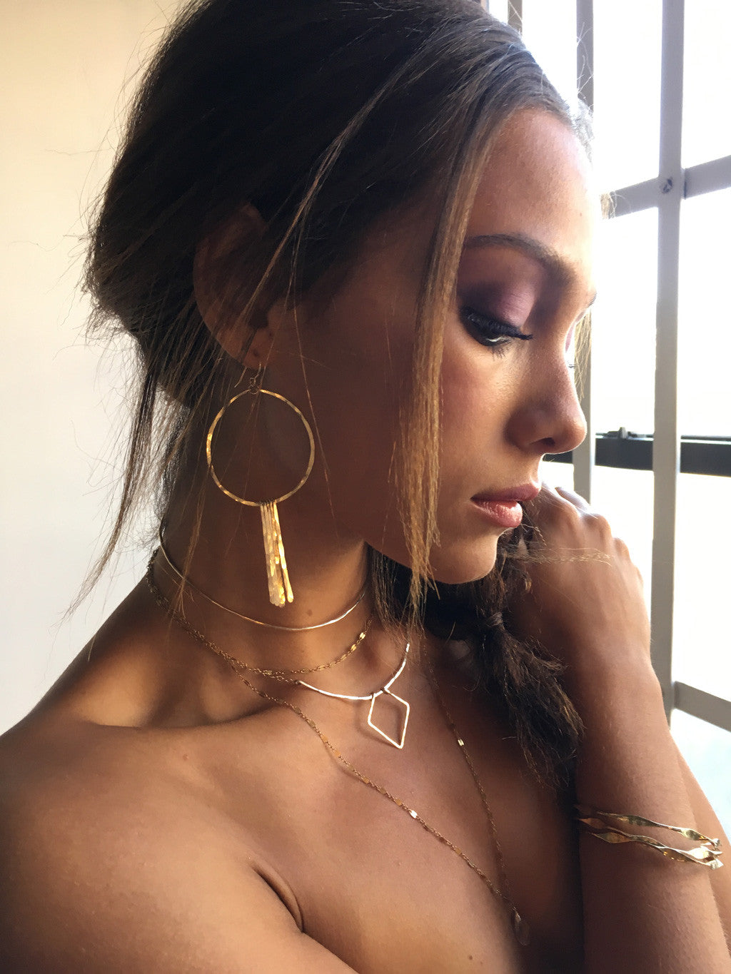 brunette looking down wearing 14k gold filled xl round fringe hoops 
