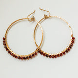 14k gold filled garnet large hoop gemstone earrings on a grey surface partially reflecting light