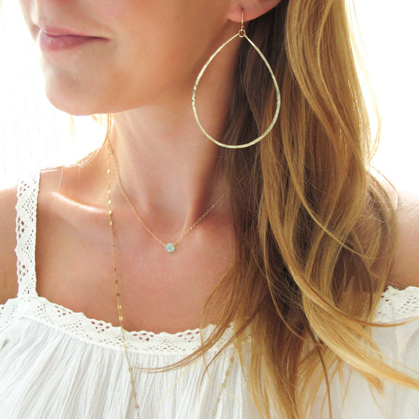 girl with large teardrop hoop earrings and delicate blue gemstone necklace
